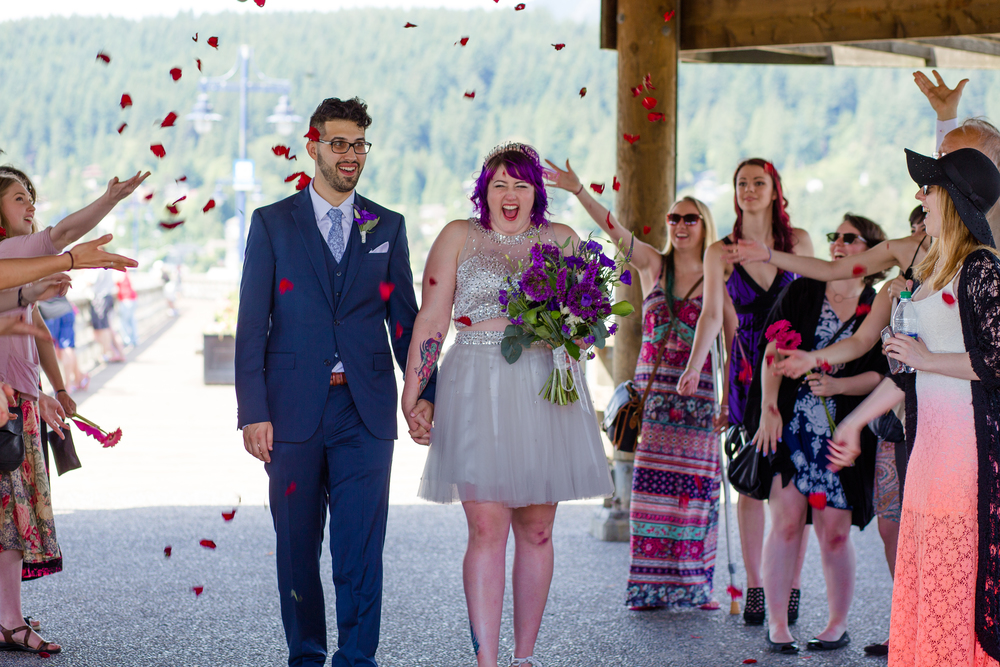 A newlywed couple walks on the covered boardwalk at Rocky Point Parkwhile their guests throw flower petals