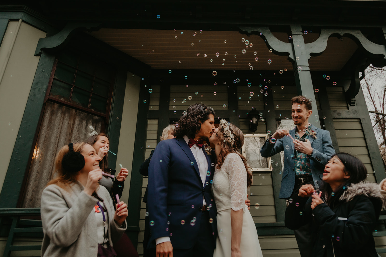 wedding party blowing bubbles and popping champagne for newlywed couple kissing