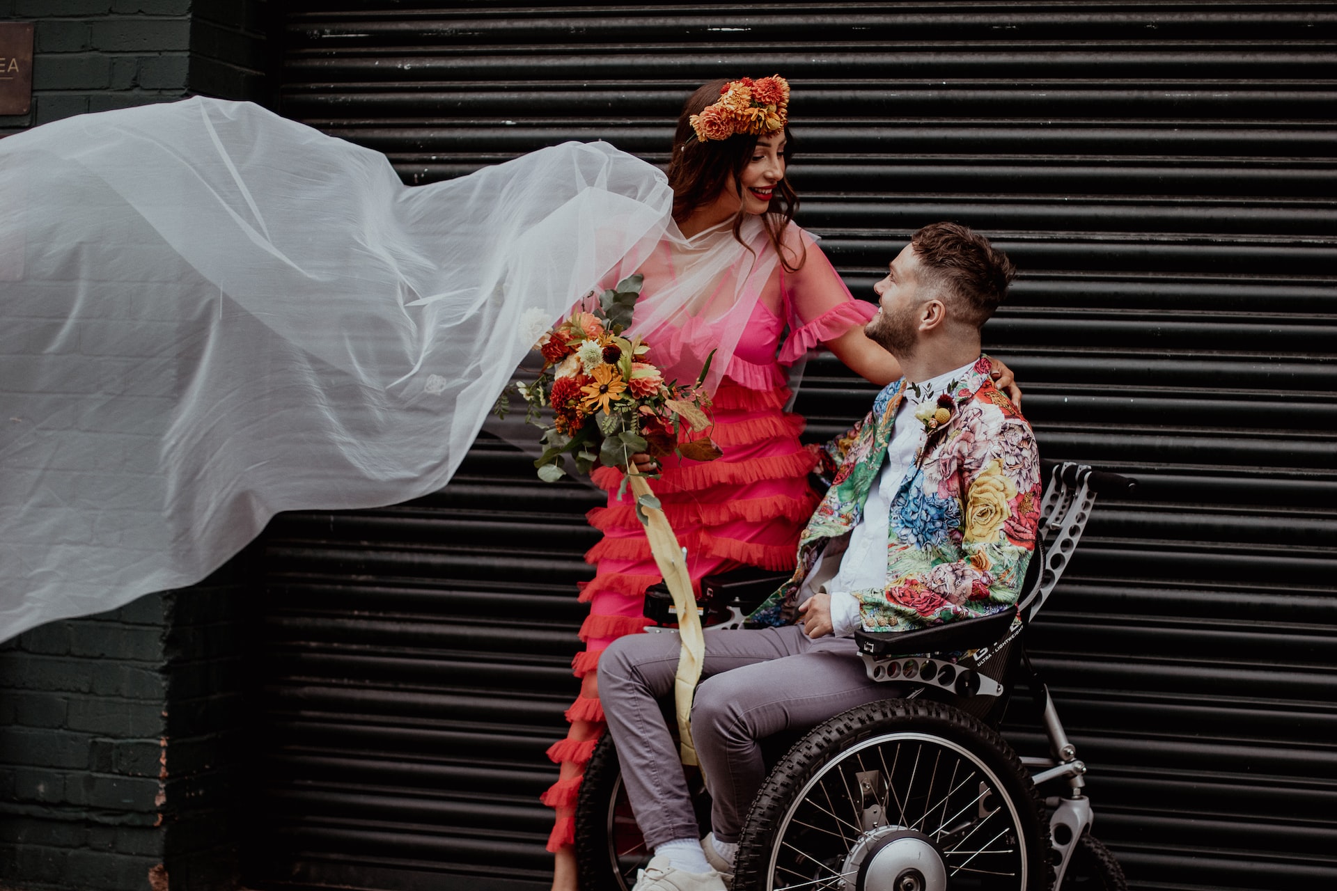 newlywed couple, bride in pink dress with veil, groom in colourful tux in wheelchair