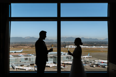 Runway Elopement at the Fairmont Vancouver Airport; silhouette of bride and groom saying their vows in front of a window overlooking the runway