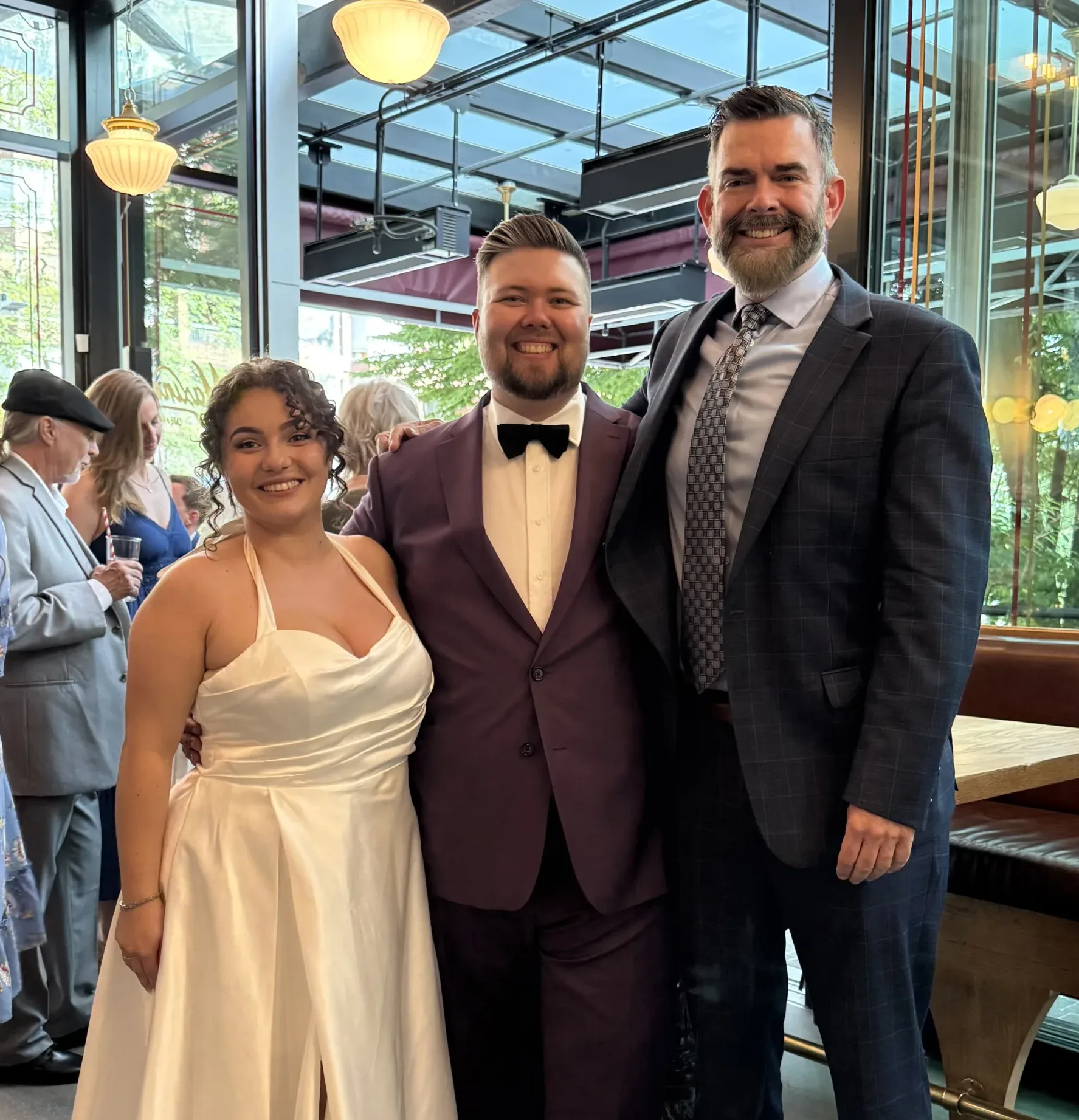 A newly-married couple in their wedding clothes pose for a photo with their Young Hip & Married wedding officiant.